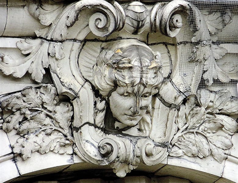 Sculpture of a person on the side of the building, with ornate carvings around it.