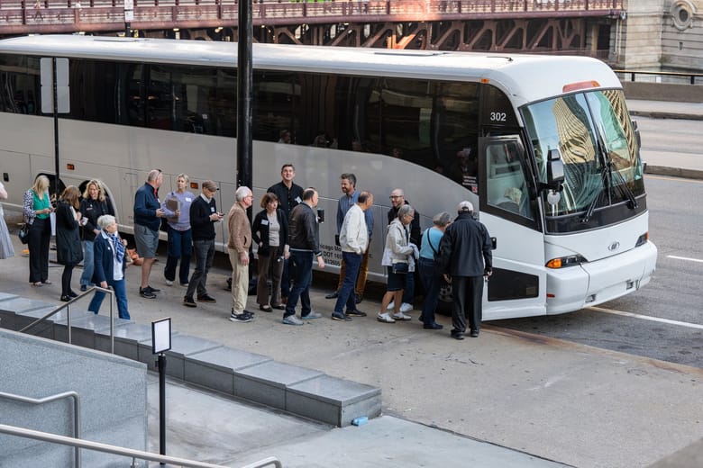 Image of a line of people standing in front of a white bus and waiting to board.