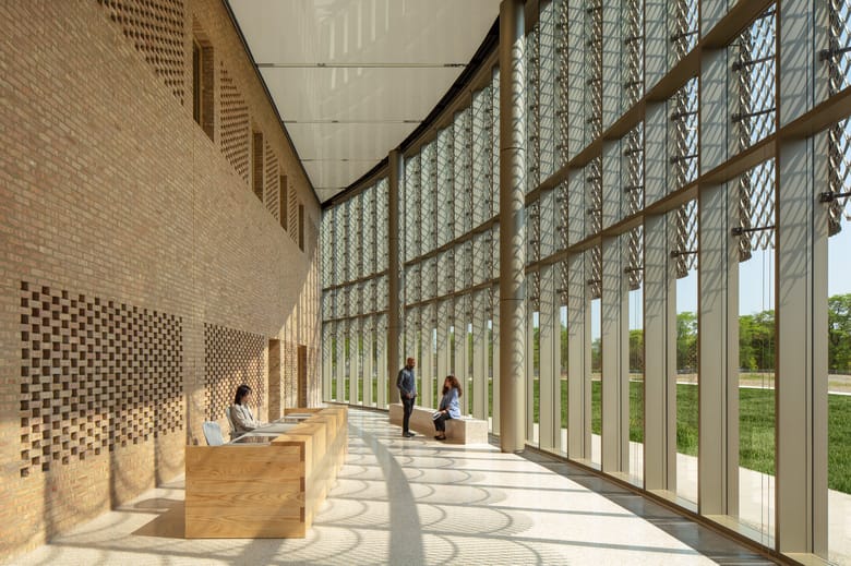 Interior of a curved buildings with a hallway that has a glass exterior wall and tall ceilings bending out of frame 