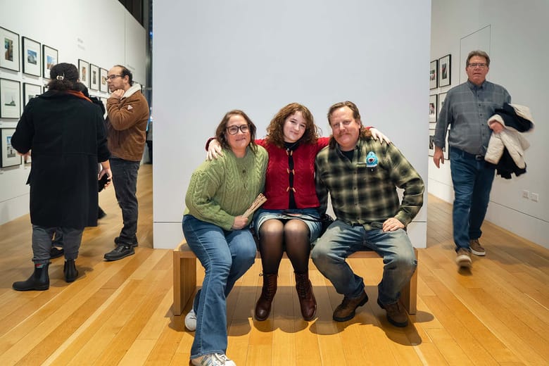 Three people seated inside an exhibition space smiling at the camera