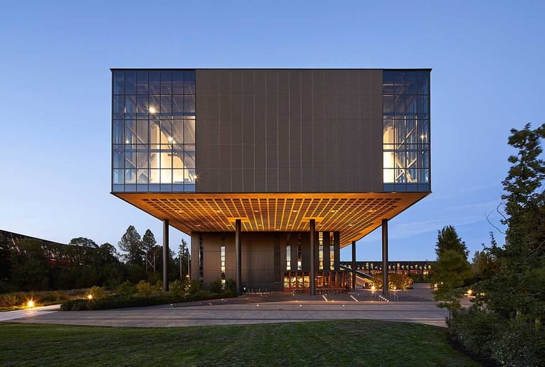 Cantilevered glass-and-steel building elevated above a landscaped campus at dusk.