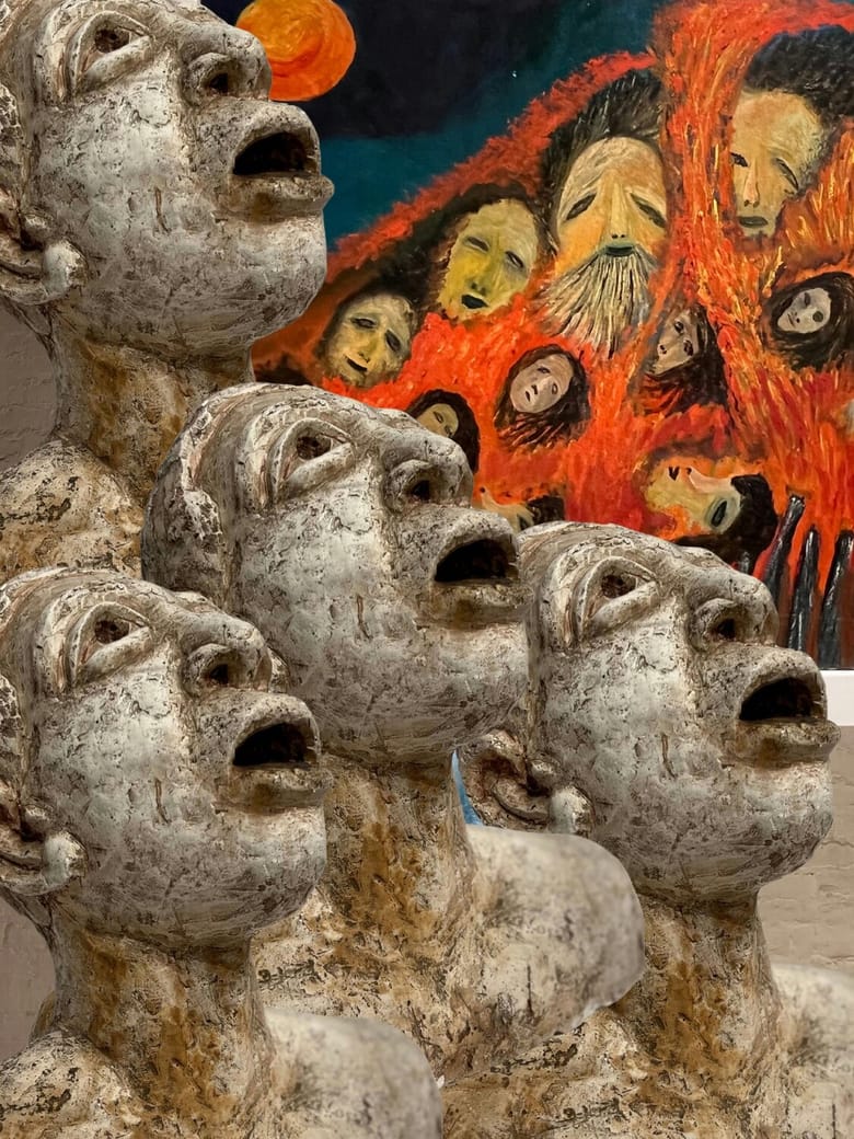 Sculptures of faces looking up and to the right with more painted faces in the back. 