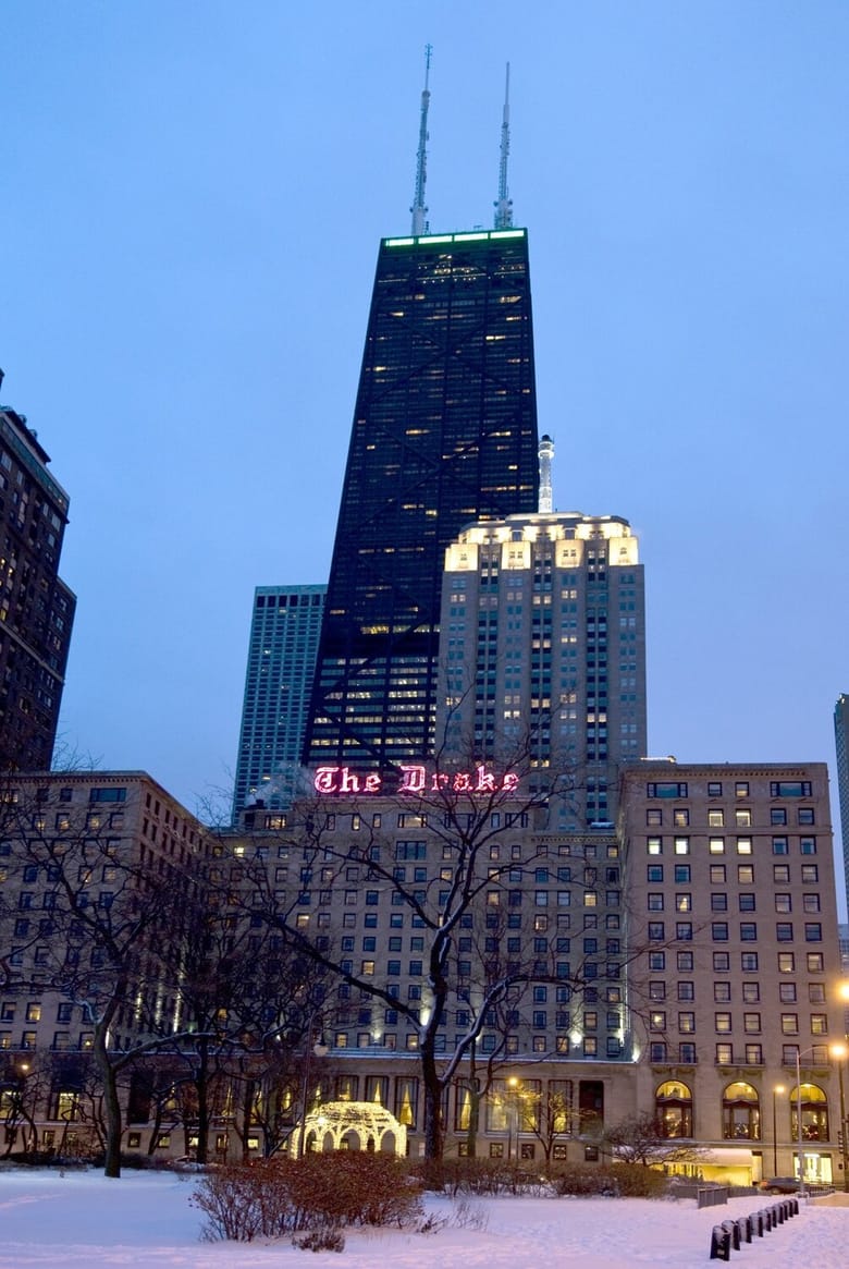 Image of a hotel building in the foreground and a tall black skyscraper in the back taken at night. 