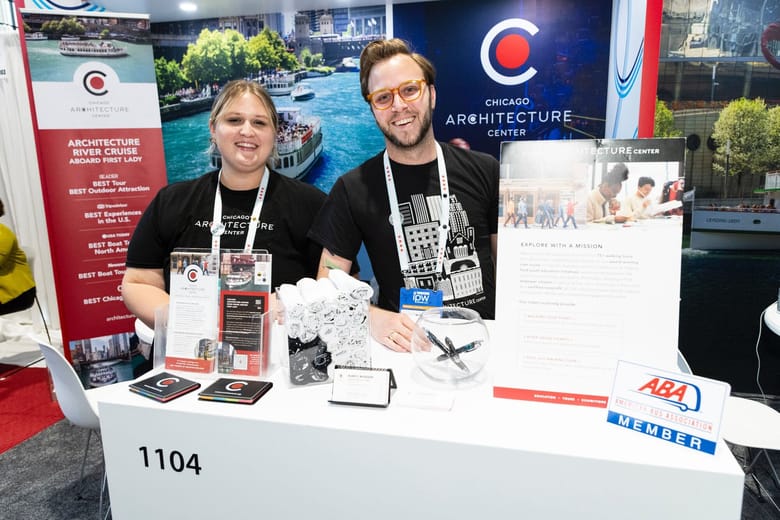 Two people stand behind a table in black shirts smiling at the camera. 