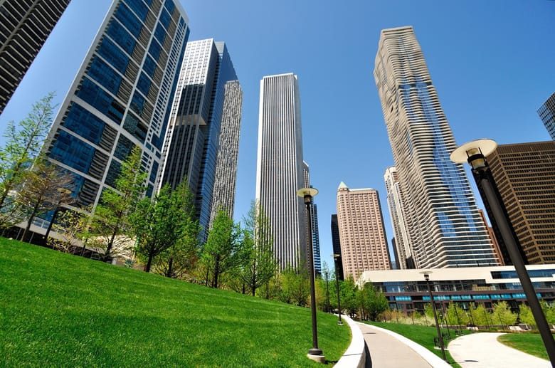 Grassy area and pedestrian path near tall city buildings.