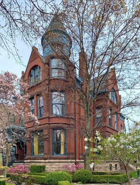 Brick victorian house behind trees.