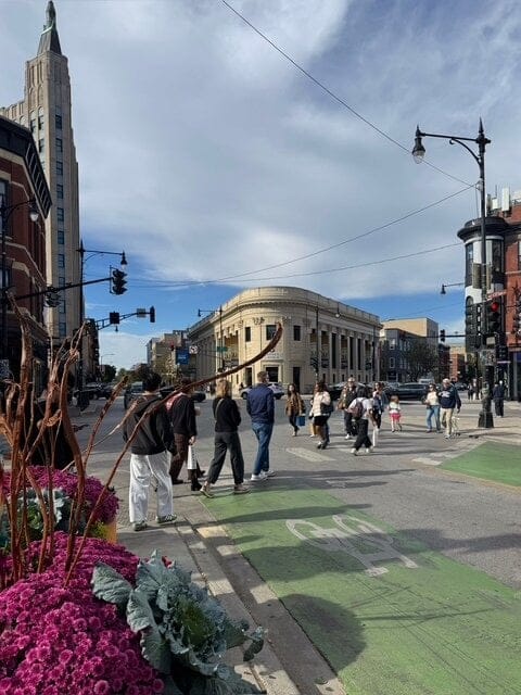 People walking through an intersection with many different surrounding buildings.