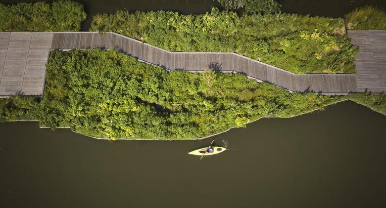 A view from above of a river with greenery on the banks and a kayak in the water. 