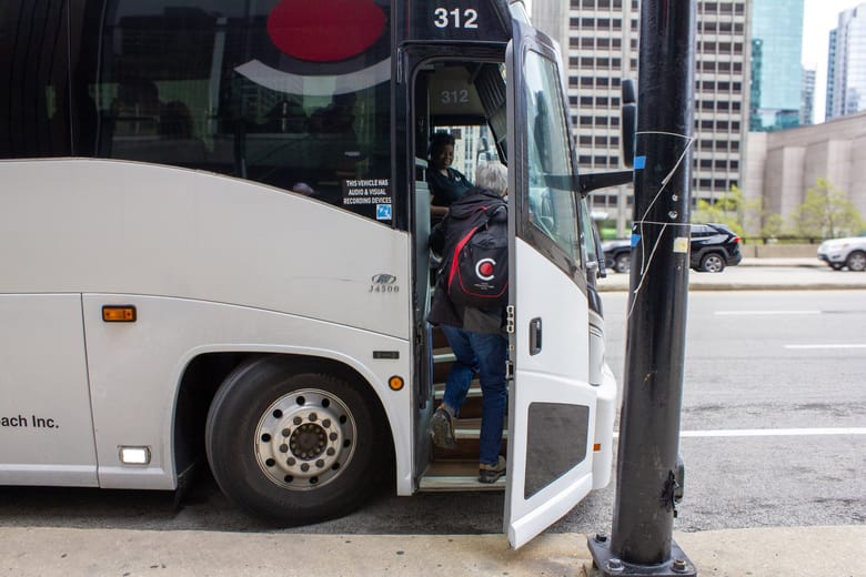 Person walking up the steps of a large white tour bus.
