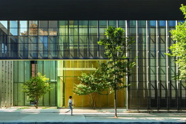 Image of a building entry with a glass facade and trees out front.