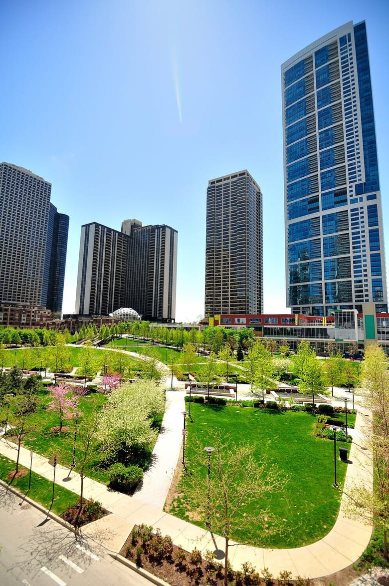Grassy area and pedestrian path near tall city buildings.