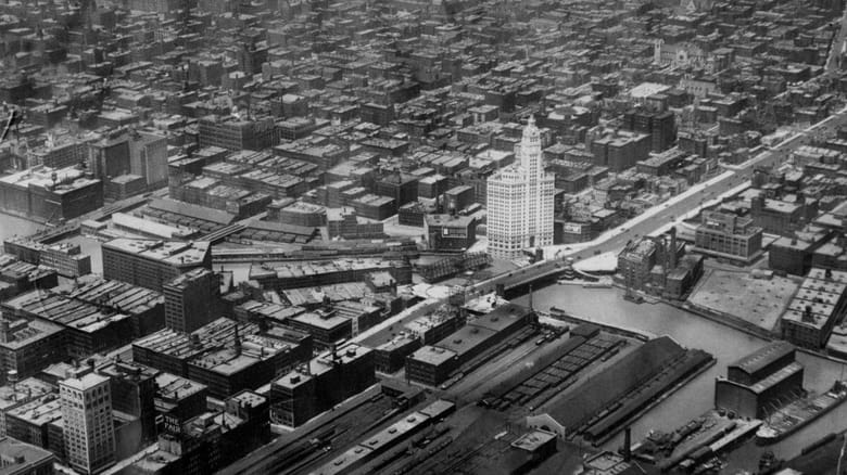 Black an white aerial image of a tall white building with a clocktower surrounded by smaller square buildings 