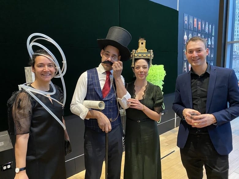 Four people stand side by side with three of them wearing costumes to resemble architecture.