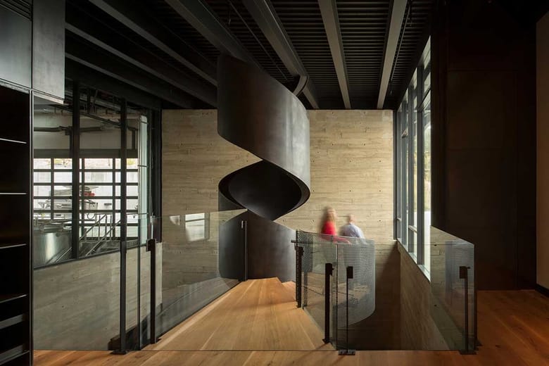 Sculptural steel spiral staircase within a concrete-and-glass winery interior.