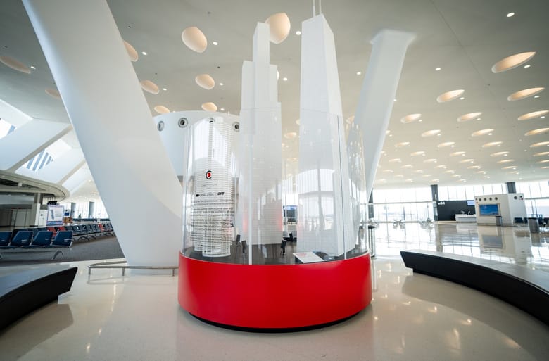 An exhibit with a red base and 3 white skyscrapers on it, in the middle of an airport.