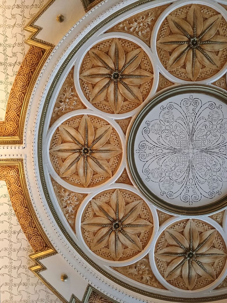 Looking up at an ornate ceiling decorated in gold and white. 