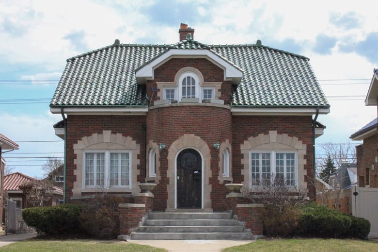 Image of a small bungalow style red brick house with a green tile roof