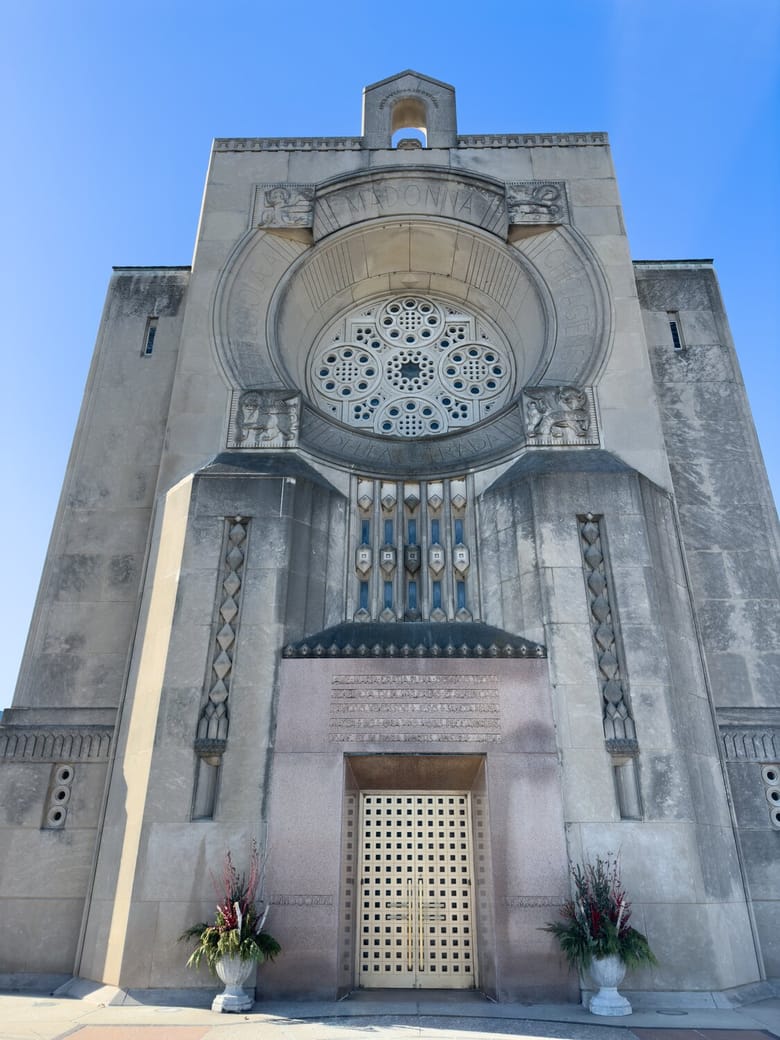 Grey stone tall building with a front door and a large circular window above it.