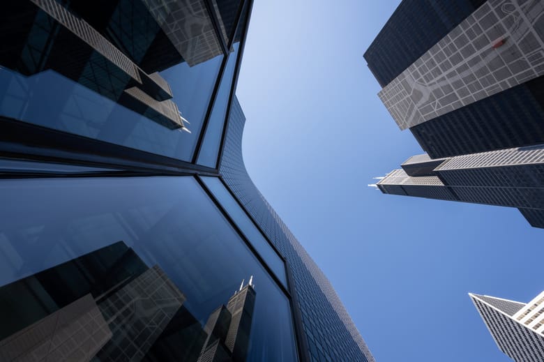 Exterior image looking up at a reflective building that curves and reflect the adjacent tall black skyscraper two times on its angled wall giving the appearance of 3 identical buildings. 