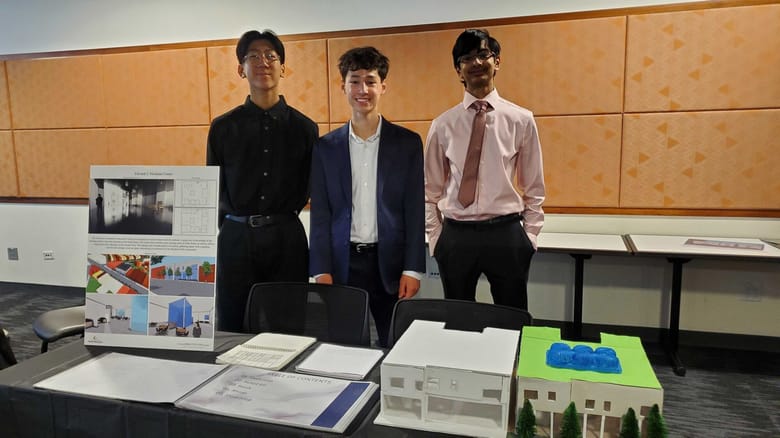 Three young men standing shoulder to shoulder behind building models sitting on a table