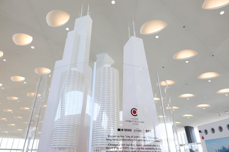 An exhibit with a red base and 3 white skyscrapers on it, in the middle of an airport.