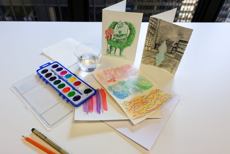 Image of water color greeting cards both standing and laying down next to paint and a cup of water
