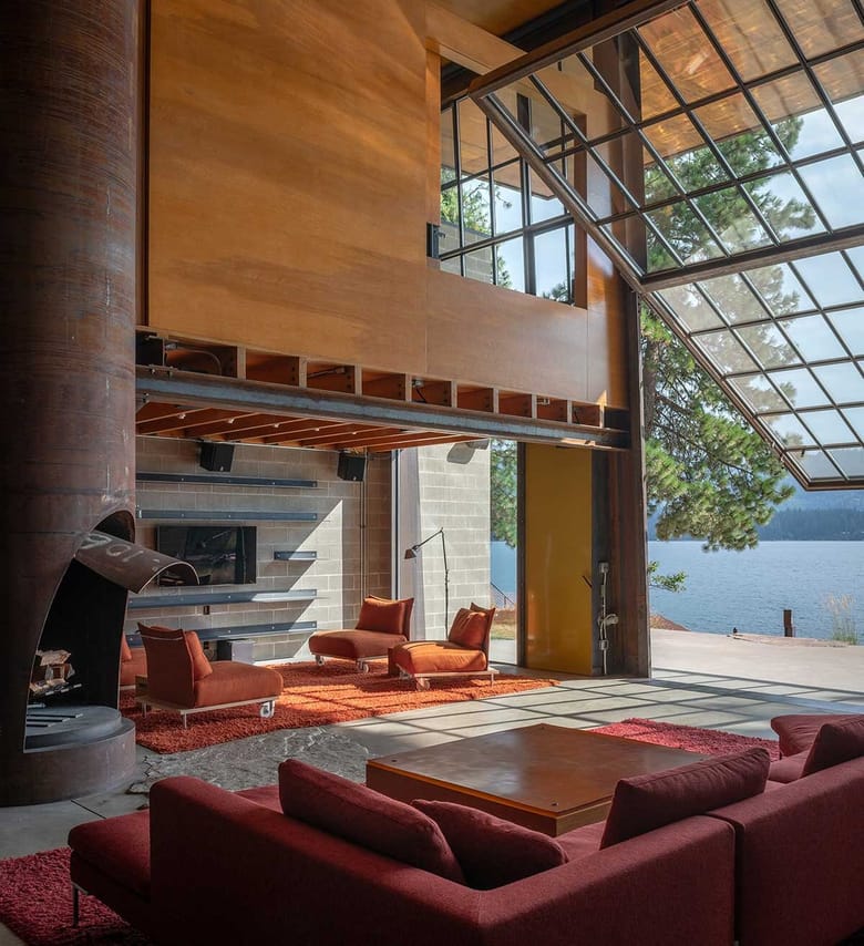 Modern lakeside cabin interior with glass walls, steel fireplace and outdoor views.