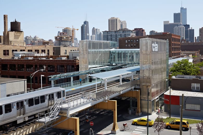 Image of an elevated train station with a train pulling in and a tall think glass structure on either side with a bridge between them.