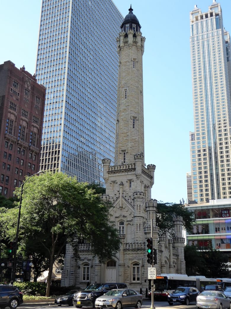 Image looking up at a tall limestone tower with skyscrapers in the background. 