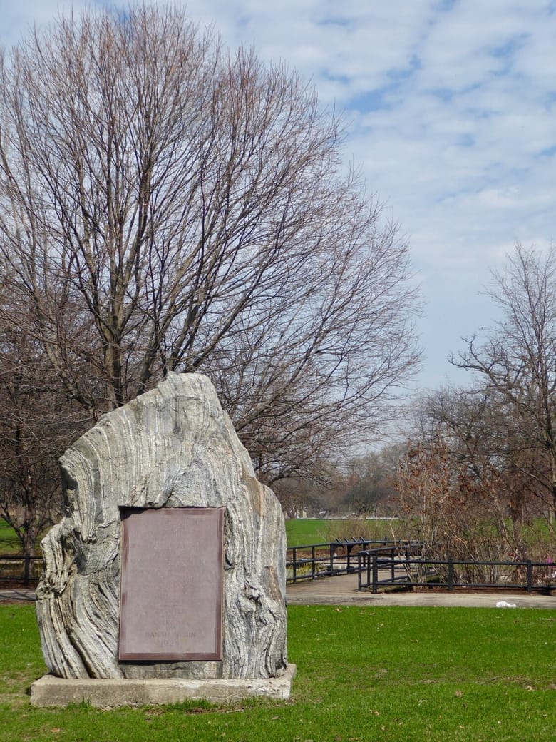 A tall rock with a plaque on its facade sitting on grass.