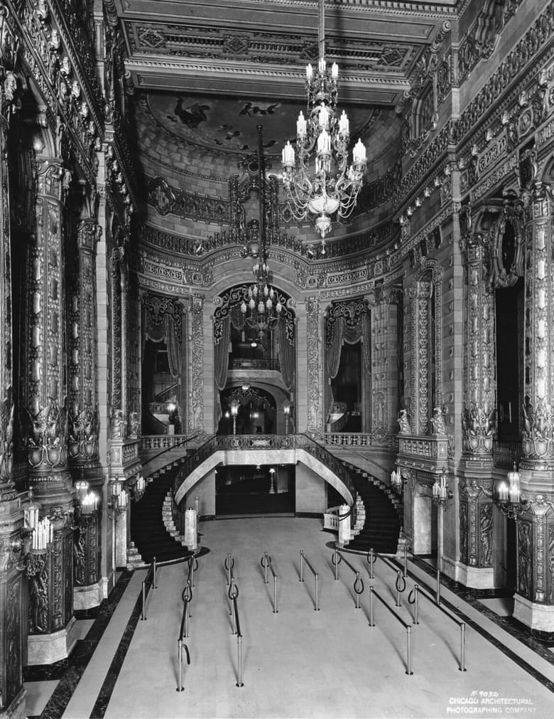 black and white image of a theater lobby with tall ceilings and hanging light fixtures. 